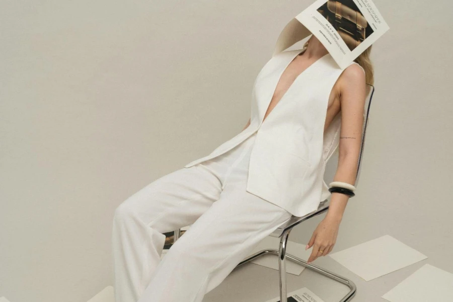Beyaz yelekli ve kırışık pantolonlu kadın yüzünde bir broşürle sandalyede yatıyor