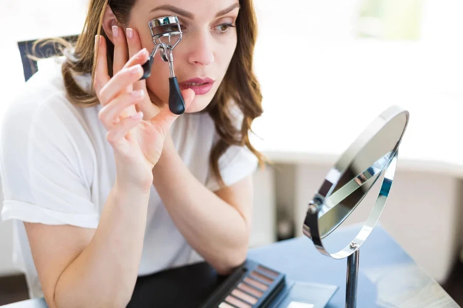 Mujer sentada frente al espejo y aplicándose maquillaje.