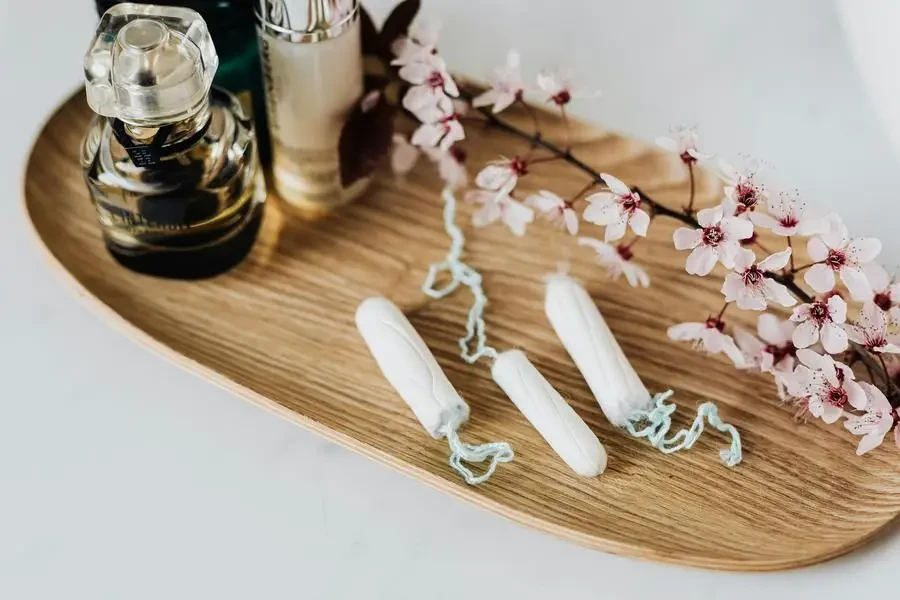 Wooden tray with perfume cosmetic products hygienic tampons and flower branch by Karolina Kaboompics