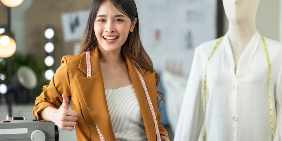 Junge asiatische Unternehmerin und Modedesignerin, die im Home-Office mit einem Laptop arbeitet