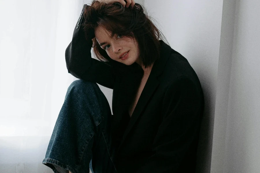 Young Woman in Black Oversized Blazer Sitting on a High Stool Fixing Her Hair