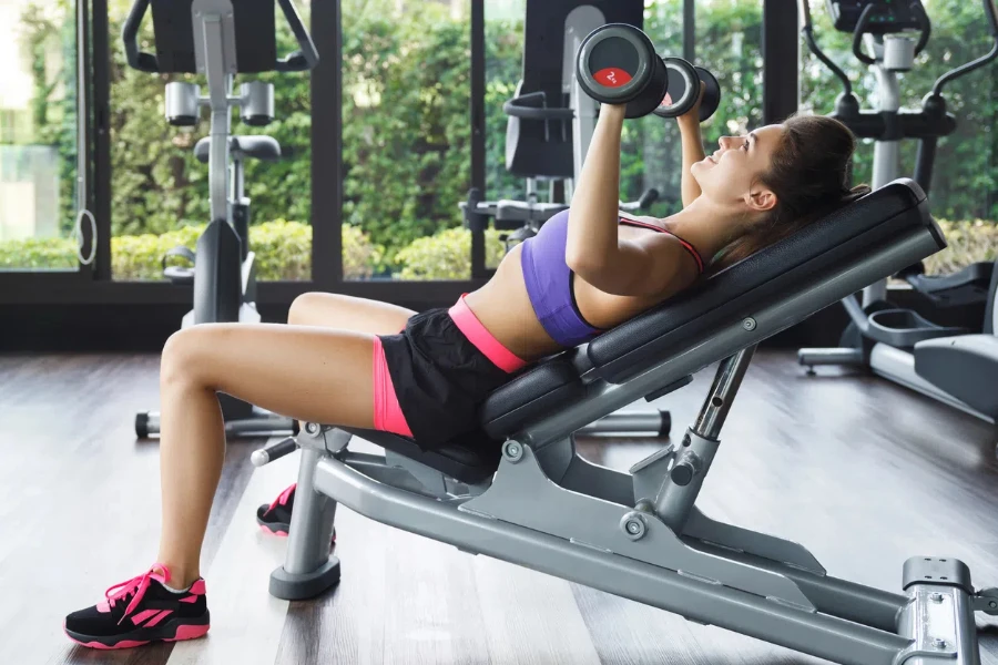 Young and beautiful woman working out with dumbbells in gym. Incline bench press exercise