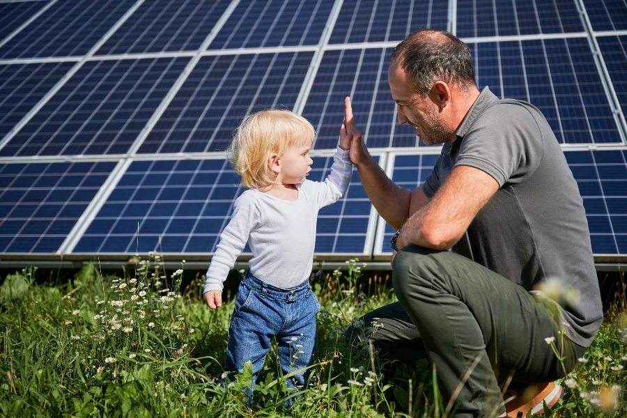 太陽光パネルを背景にハイタッチをする若い父親と幼い息子