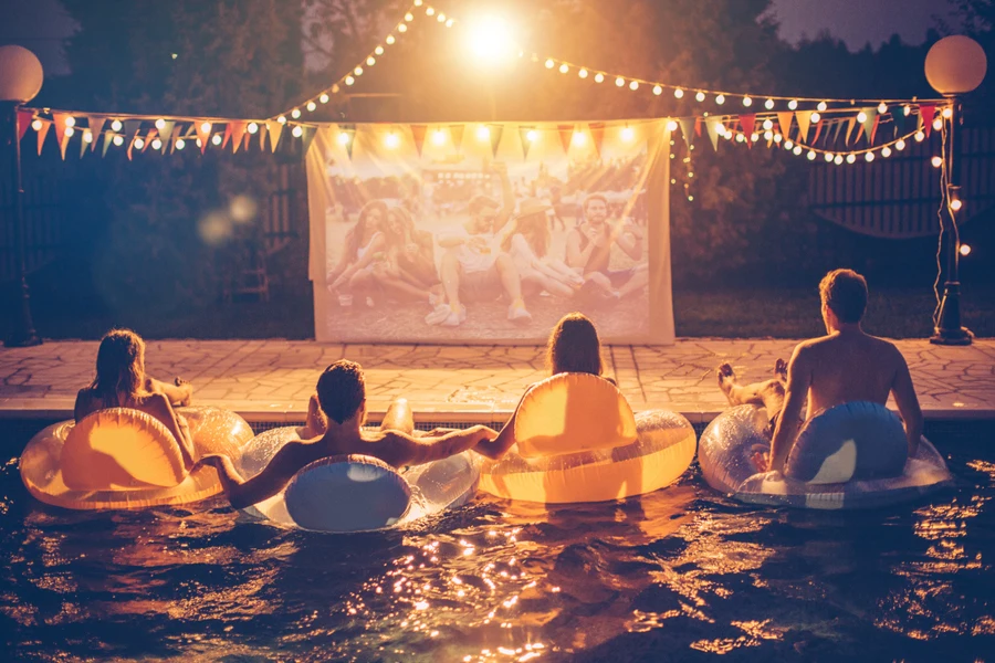 Jóvenes amigos teniendo una fiesta nocturna de cine en la piscina