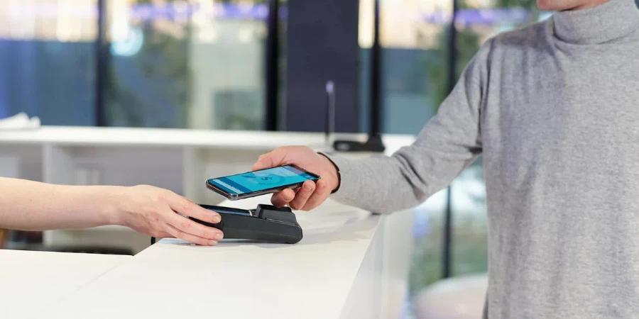Pemuda pullover abu-abu memegang smartphone dengan halaman perbankan online di layar
