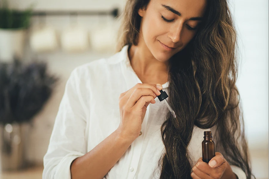 Young woman applying natural organic essential oil on hair and skin