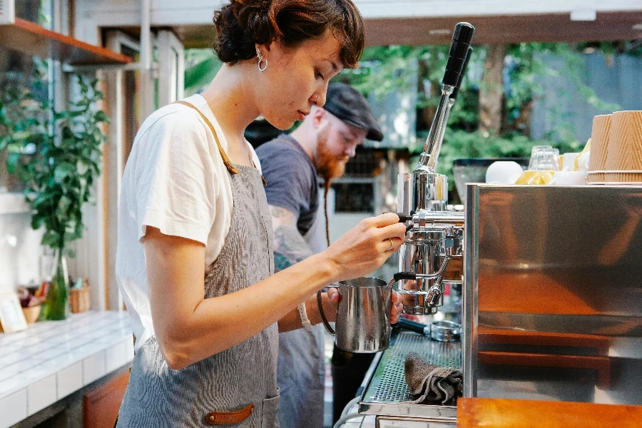 Young woman in apron using coffee machine