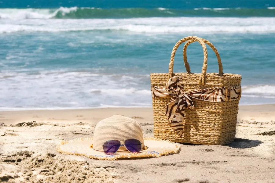 Kenarlı şapkanın yanında kahverengi dokuma plaj çantası