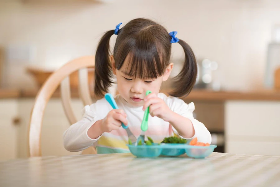 une fille utilise son ustensile spécialement conçu pour que les enfants mangent