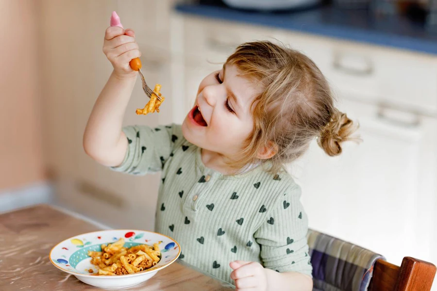 uma linda garota aprende a comer com o garfo do seu filho