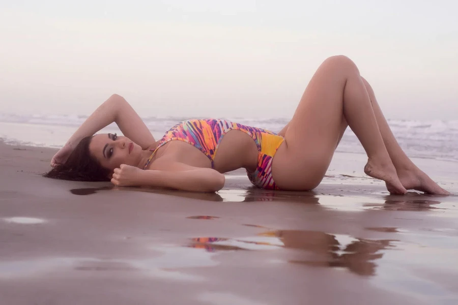 A woman in a printed one-piece swimsuit lying on the beach