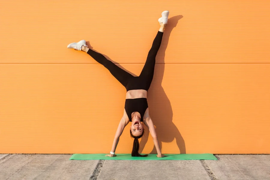 Chica haciendo yoga pose de pino contra la pared y riendo