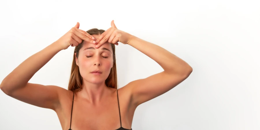 tiro na cabeça retrato jovem adulto mulher caucasiana fazendo ioga massagem facial na testa fundo isolado no branco