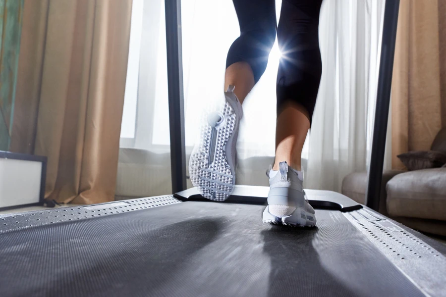 Gambe di una ragazza in scarpe da ginnastica che corre su un simulatore di tapis roulant