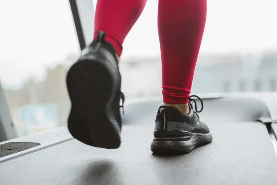 Legs of woman running on treadmill in light gym closeup