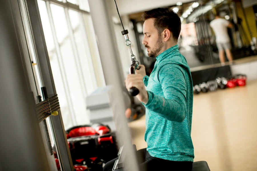 رجل وسيم يمارس التمارين الرياضية على آلة اللات في صالة الألعاب الرياضية