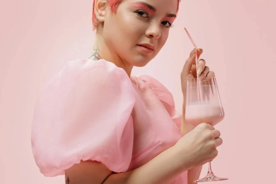 Una mujer vestida de rosa sosteniendo un vaso transparente con batido