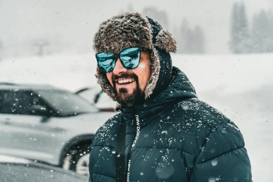 雪が降る中、車のそばで中綿入りジャケットを着て微笑む男性