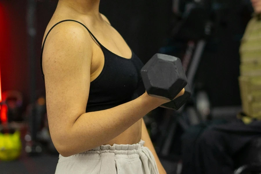 Seorang Wanita Berbaju Crop Top Hitam Mengangkat Dumbbell