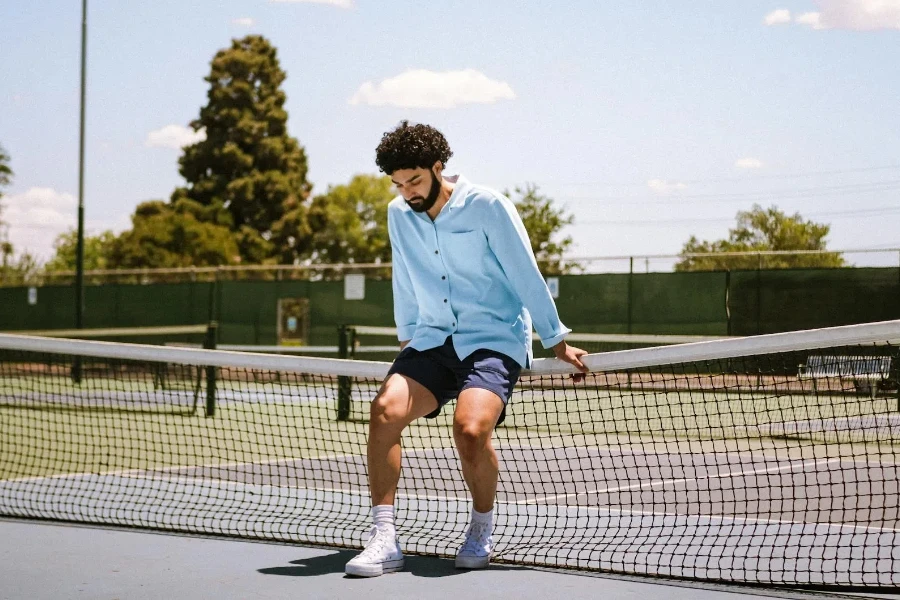 Mann sitzt auf Tennisplatznetz