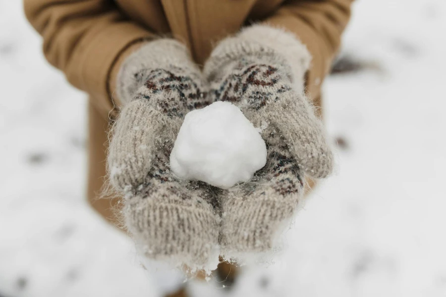 Person trägt gestrickte Handschuhe und hält einen Schnee