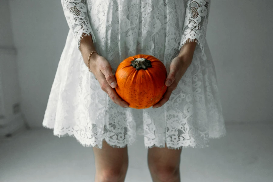 Woman in White Lace Long Sleeve Dress Holding Pumpkin
