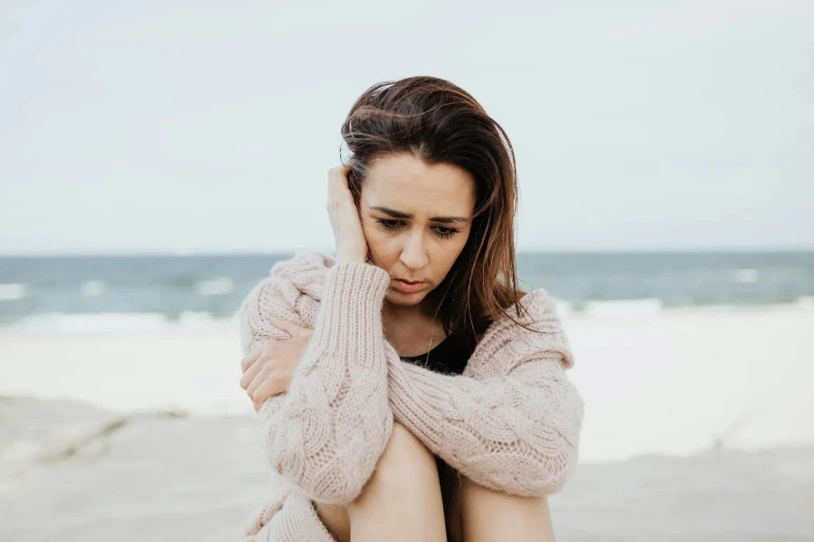 Donna in maglione rosa che si siede sulla spiaggia