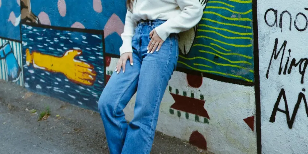 Wanita dengan jeans longgar bersandar di dinding