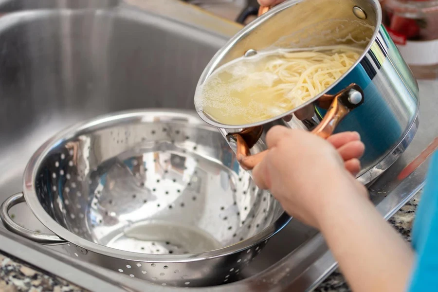 woman separating water from spaghetti withempty silver colander