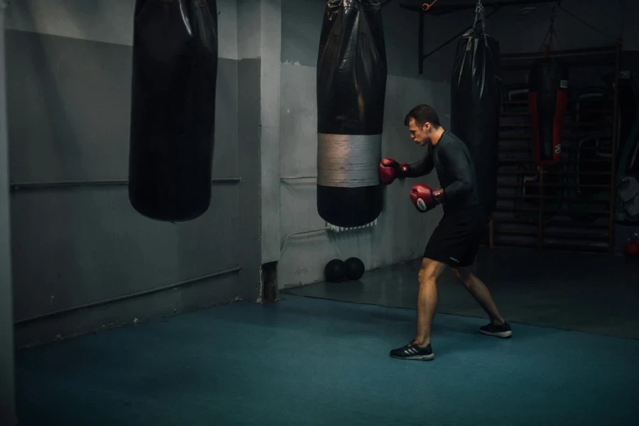 Un homme en manches longues noires portant des gants de boxe tout en frappant un sac