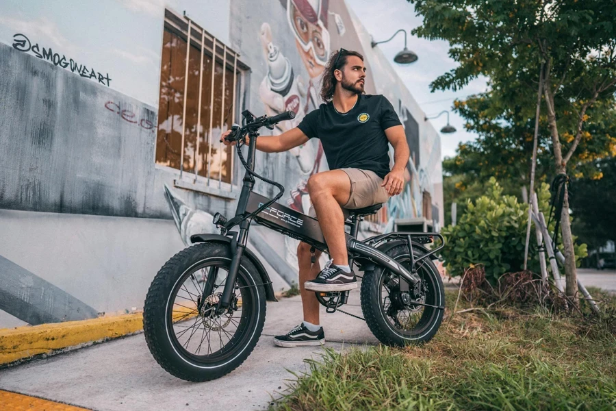 Um homem de camisa preta andando de bicicleta elétrica na rua