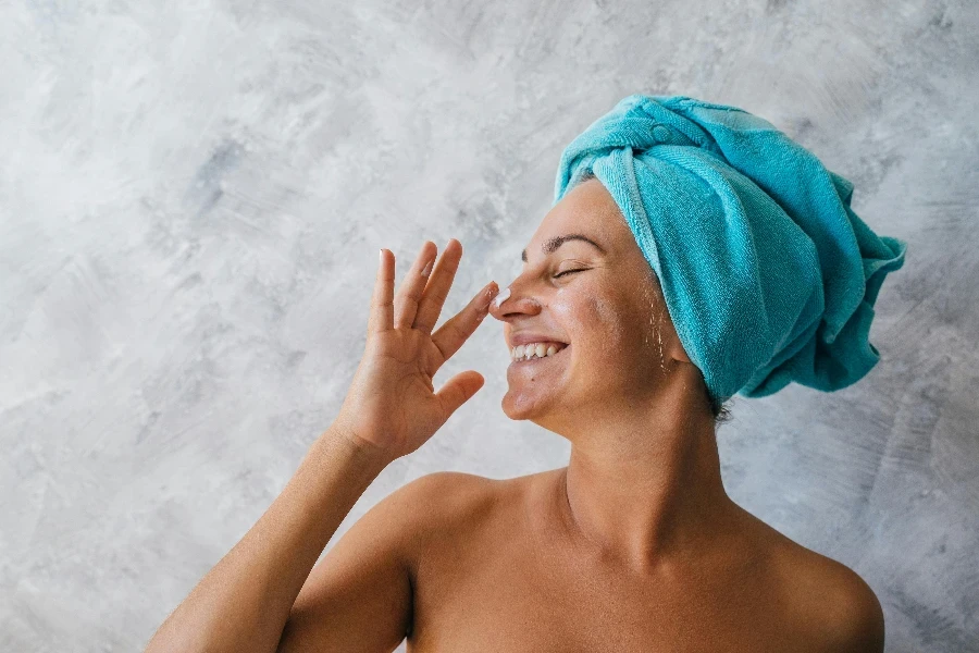 Une femme souriante appliquant de la crème pour le visage sur son nez