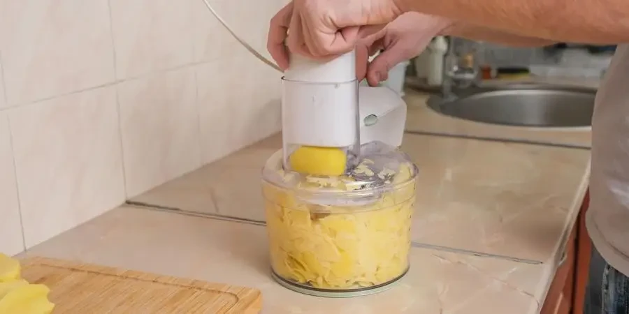 A man cuts potatoes into thin slices in food processor. Preparation of potatoes for cooking