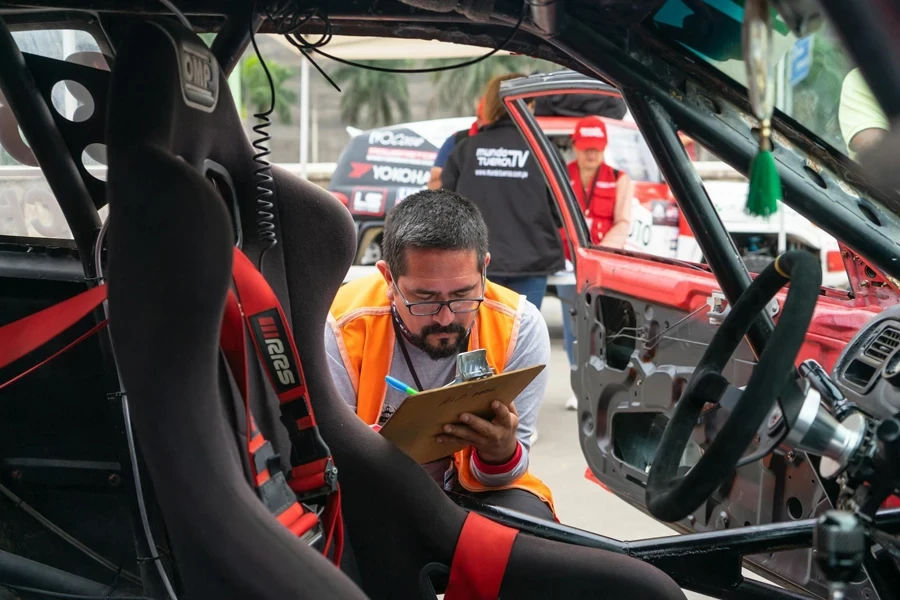 A man in an orange vest is looking at a car