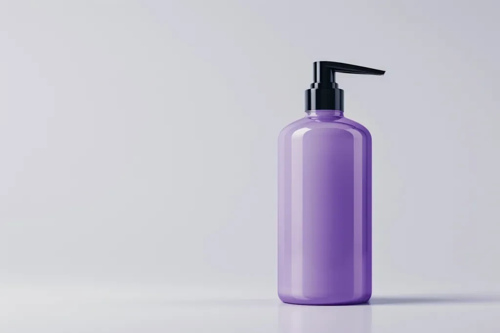 Um frasco de xampu roxo simples e curto com uma bomba preta sobre um fundo branco