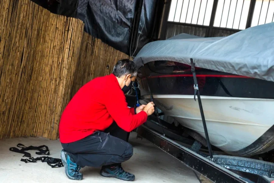 Ein erwachsener Mann mit Schutzmaske überprüft die Befestigungsgurte eines Motorboots in der Garage