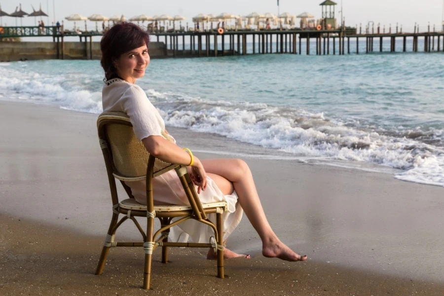 Een volwassen vrouw op het strand zit op een stoel en kijkt naar de zee