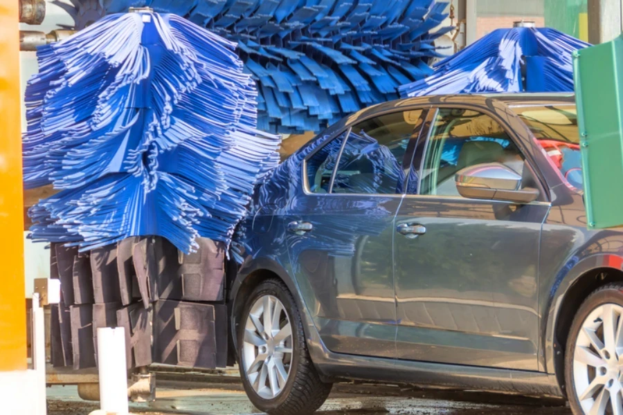 Cepillo azul de lavado automático en acción, el auto gris sale listo y limpio