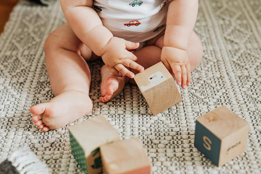 Baby sitzt auf Teppich und spielt mit Holzklötzen