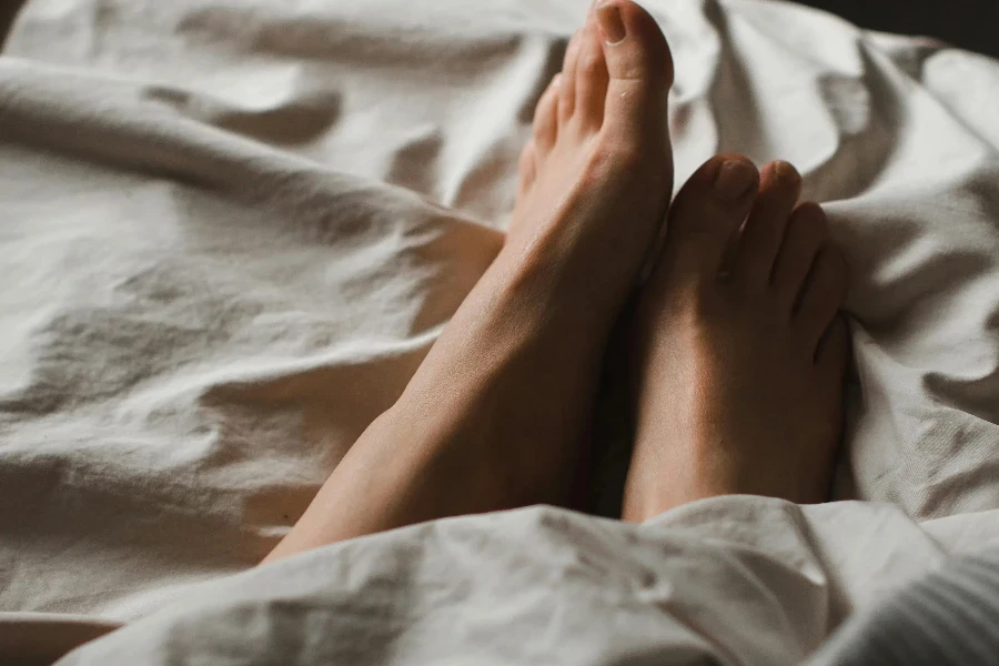 Crop anonymous barefoot female feet relaxing on soft comfy bed