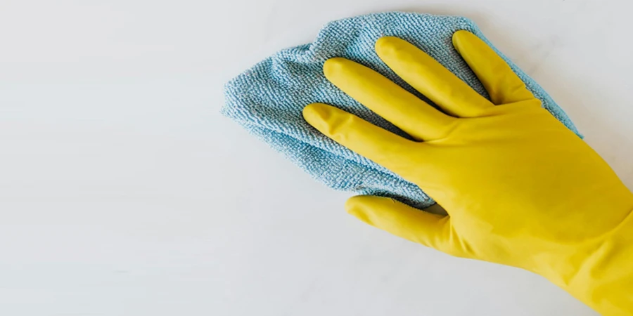 Crop unrecognizable person in yellow gloves cleaning white surface