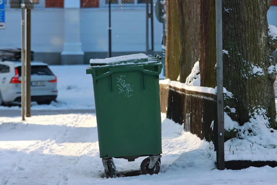 Lixeira verde em uma rua com neve