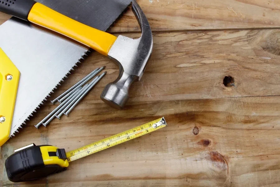 Hammer, saw, nails and tape measure on wood.