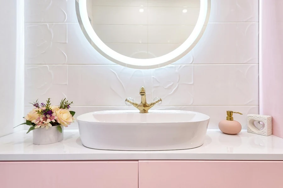 Interior de un baño moderno con espejo luminoso colgado debajo del lavabo con grifo cerca de flores y jabón