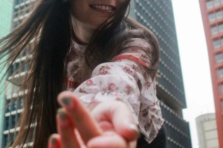 Vriendelijke vrouw in roze blouse die haar hand naar de camera laat zien