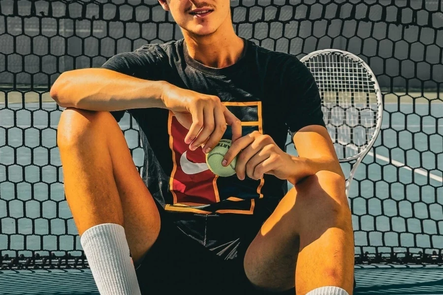 Man in T-Shirt and Shorts Sitting by Net at Tennis Court