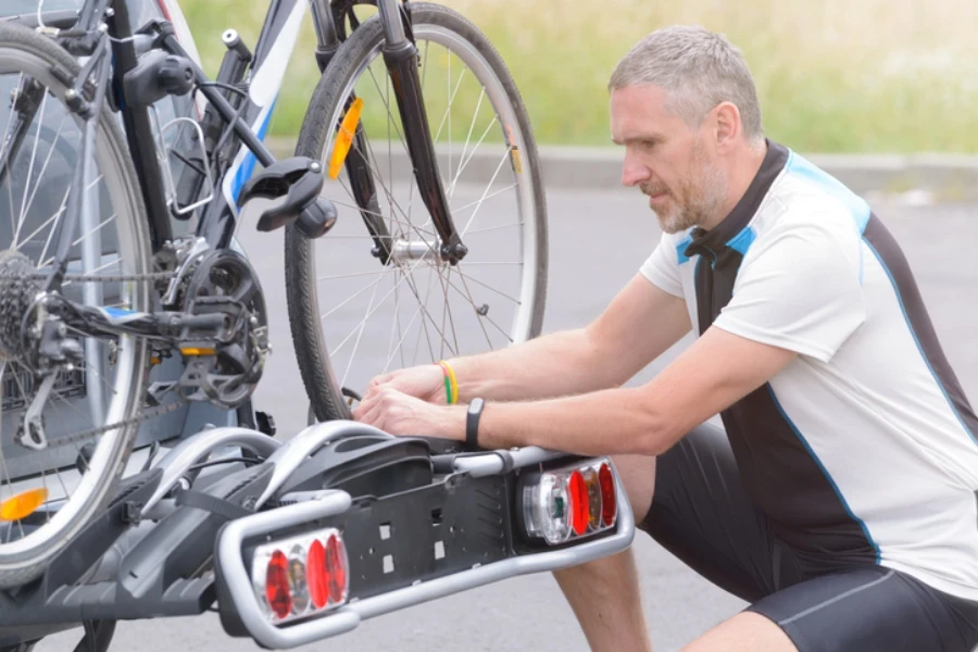 Uomo che indossa abbigliamento sportivo e carica biciclette sul portabiciclette montato sul gancio di traino di un'auto