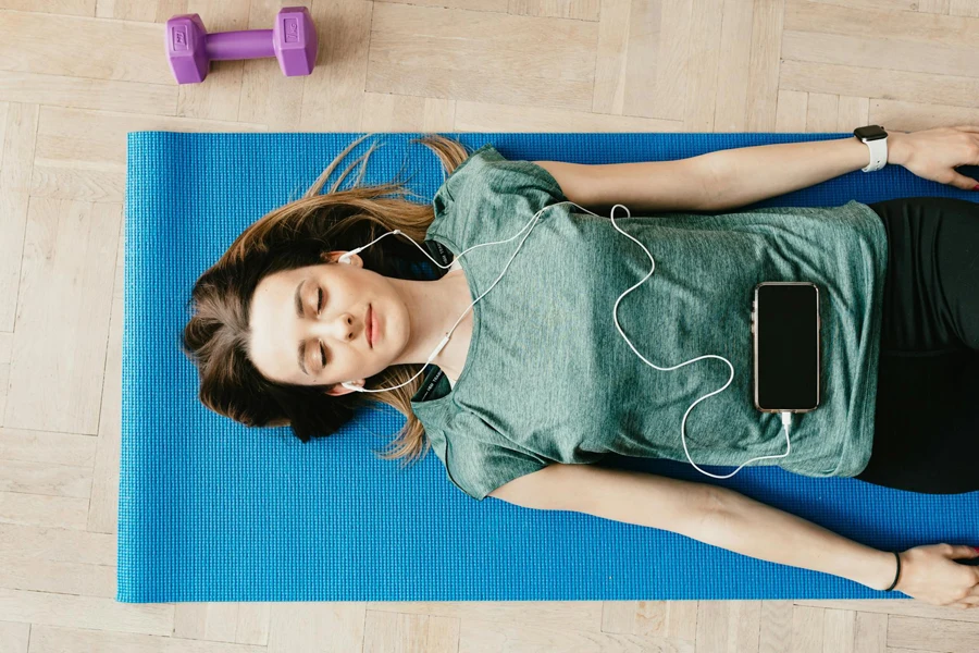 Friedliche Frau mit Kopfhörern ruht sich zu Hause in Shavasana-Pose aus