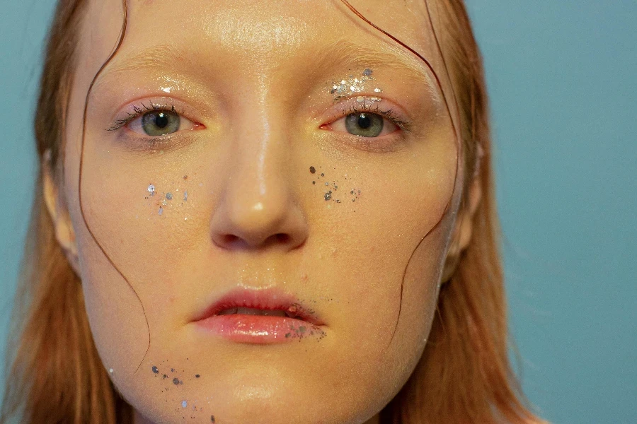 Jeune femme sérieuse avec des paillettes sur le visage regardant la caméra en studio