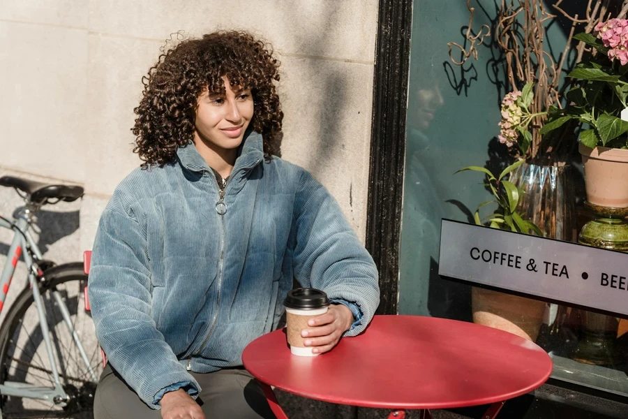 Lächelnde ethnische Frau mit Coffee to go im Straßencafé